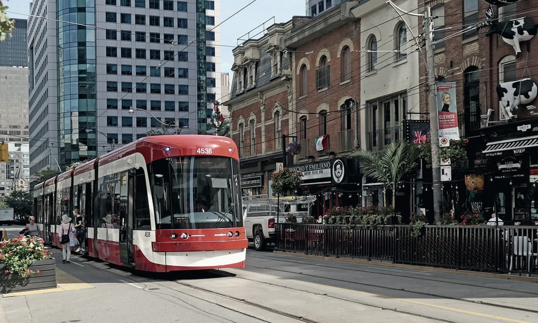 A red TTC streetcar passing small storefronts on a Toronto street